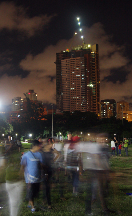 Spectators of a rock concert against the pork barrel system appear ghostly as they mill about the sprawling park.  The city's ever-changing skyline also put up a complementary show.  (Rizal Park, Manila)
