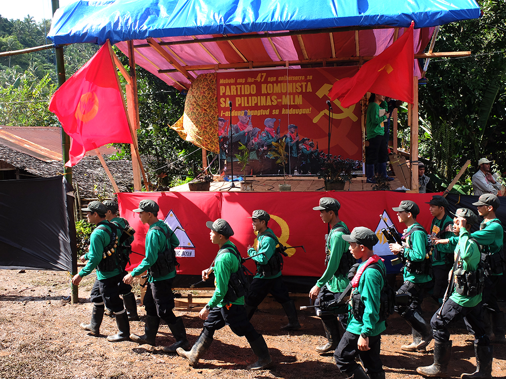 New People's Army fighters walk before their movement's standards as they take their positions for the start of the Communist Party's anniversary celebrations. (Kitcharao, Agusan del Norte)
